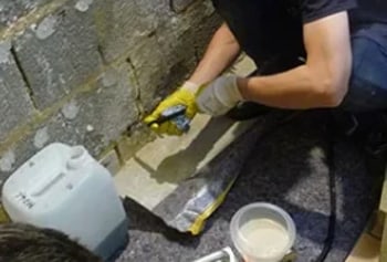 Eine Person in Handschuhen füllt eine Fuge in einer Steinmauer mit Dichtmittel.