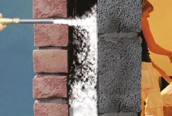 Isolierung einer Ziegelwand mit einer Sprühdüse, die Dämmmaterial in den Hohlraum bläst.