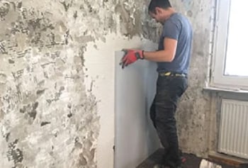 Ein Mann in blauer Kleidung bringt eine weiße Platte an einer unfertigen Wand an.
